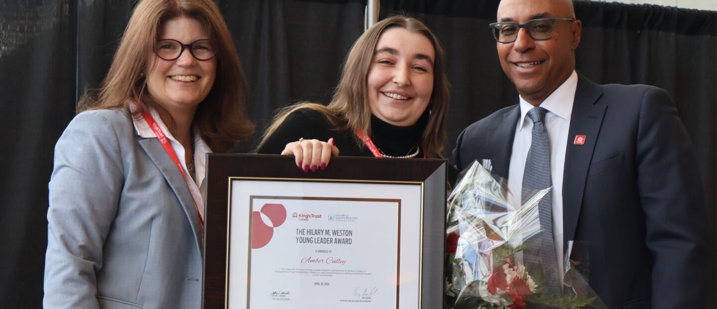 Three people stand together with a certificate and bouquet of flowers, smiling.